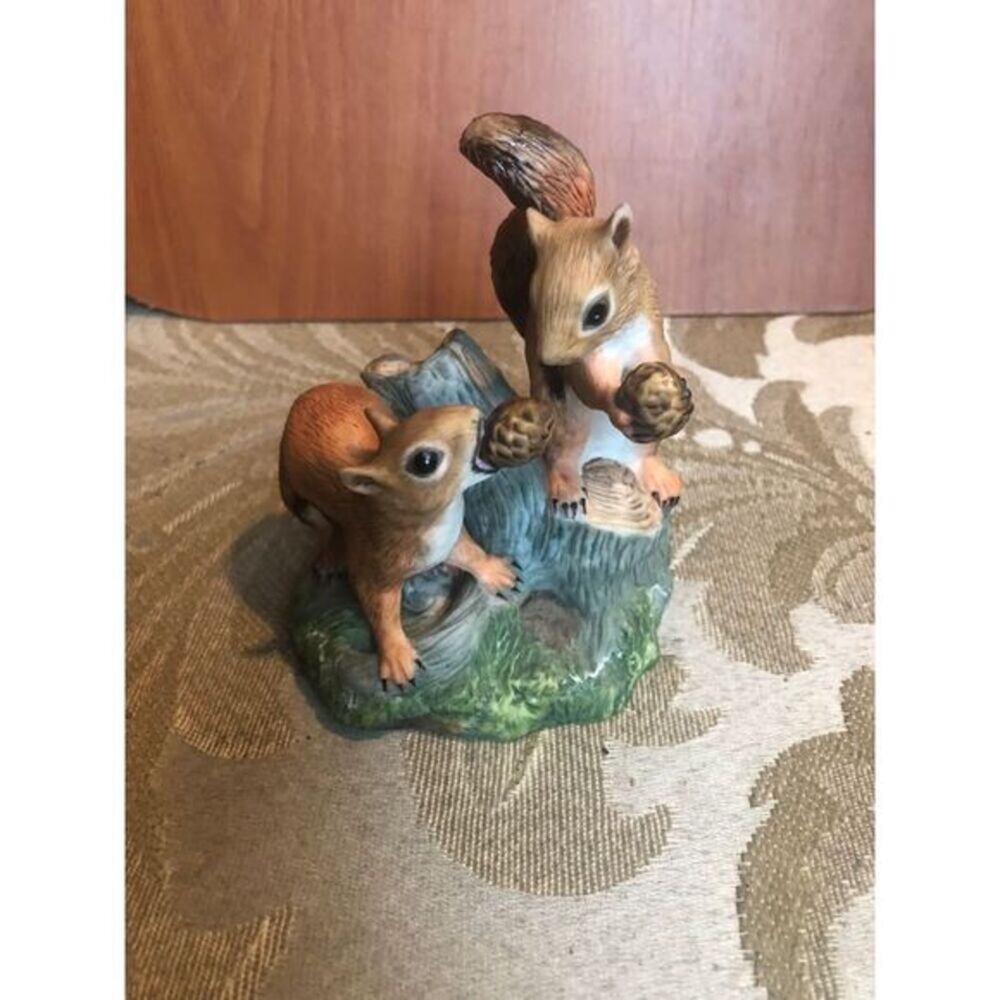 Ceramic figurine of two squirrels sitting on a tree stump holding pine cones.